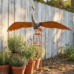 A large metal bird sculpture with orange wings perched on a metal stand, surrounded by potted plants in a garden setting.