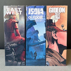 Peut inclure: Trois couvertures de romans graphiques. La première couverture est rouge et noire avec le titre "East of West". La deuxième couverture est bleue et blanche avec le titre "1591A Outpost Zero". La troisième couverture est marron et orange avec le titre "Gideon Falls".