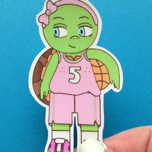 May include: A pink and green cartoon turtle wearing a pink basketball jersey with the number 5 on it. The turtle is holding a basketball and has a pink bow in its hair.
