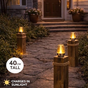 May include: Solar-powered garden lanterns featuring three square wooden posts with rope accents and glass tops. Each post is 40 cm tall and emits a warm glow. The text reads: SOLAR-POWERED GARDEN LANTERNS, 40CM TALL, CHARGES IN SUNLIGHT, LIGHTS UP AT NIGHT.