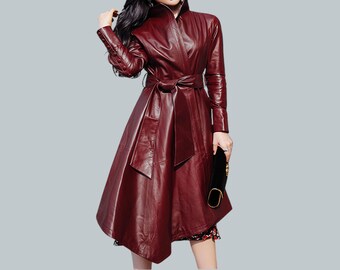 May include: A burgundy leather trench coat with a belted waist and a flared skirt. The coat has a collar and long sleeves.