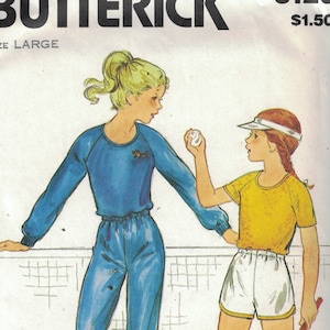 May include: A vintage sewing pattern for a women's athletic outfit. The pattern is for a blue and white tracksuit with a long-sleeved top and matching pants. The pattern also includes a yellow short-sleeved shirt and white shorts. The pattern is size large and is for moderate stretch knits only. The pattern number is 3120 and the price is $1.50.