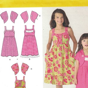 May include: Simplicity sewing pattern 1703 HH for girls' dresses and a cardigan. The pattern includes two dress styles, one with a floral print and one in solid pink. Both dresses have a gathered skirt and a lace trim. The cardigan is a simple, short-sleeved style.