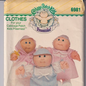 Peut inclure: Un patron de couture vintage pour les bébés Cabbage Patch Kids. Le patron est destiné à la confection de vêtements pour les poupées Cabbage Patch Kids. Le patron est de la marque Butterick et porte le numéro 6981. Le patron montre trois poupées Cabbage Patch Kids portant des tenues différentes.