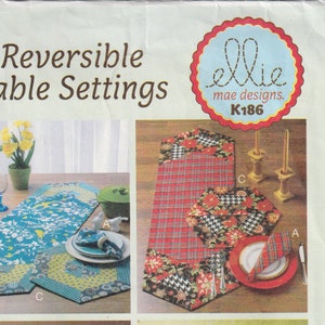 May include: Two reversible table runner sets, one with a blue and white floral pattern and the other with a red and black plaid pattern. Each set includes a table runner and two placemats. The pattern on each side of the table runner and placemats is different. The image includes the text "Reversible Table Settings" and "K186".