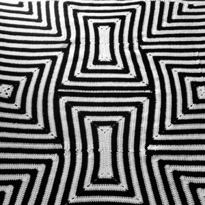 May include: Black and white crocheted blanket with a geometric pattern. The design features concentric squares and rectangles, creating a bold, graphic effect. The alternating black and white stripes give the blanket a modern, eye-catching look. The blanket is handmade.