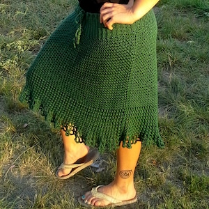 May include: A green crochet skirt with a scalloped hem. The skirt is made with a simple stitch pattern and has a tie at the waist.