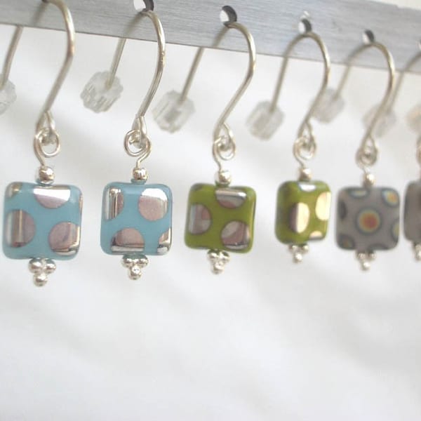 May include: A set of eight silver earrings with square glass charms. The charms have different patterns, including blue and white polka dots, green and white polka dots, and gray and white geometric patterns.