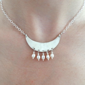 May include: A silver necklace with a crescent moon pendant and a row of white pearl drops.