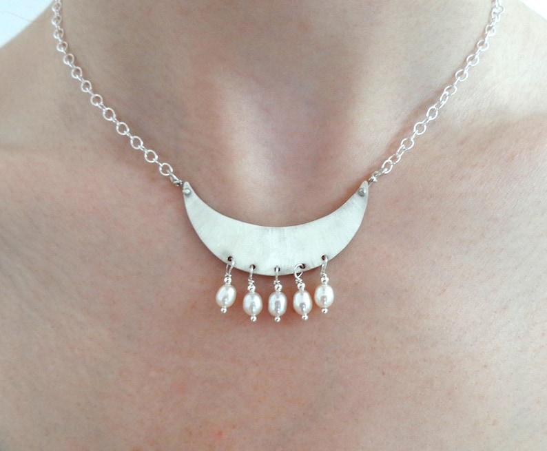 May include: A silver necklace with a crescent moon pendant and a row of white pearl drops.