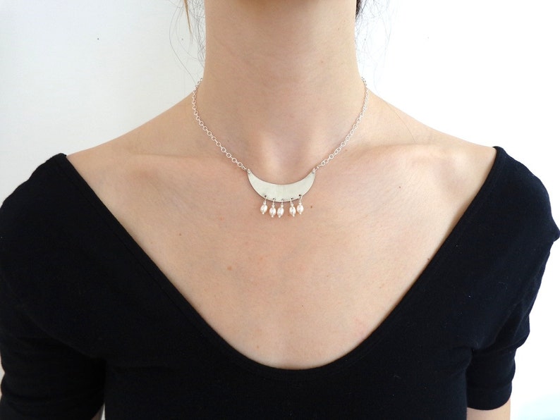 May include: A silver necklace with a crescent moon pendant and small pearl accents.