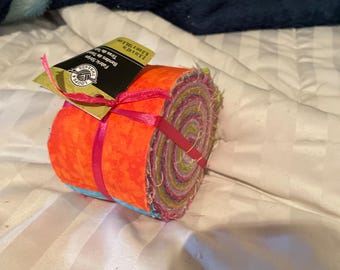 May include: A roll of colorful fabric strips, wrapped with a bright pink ribbon. The fabric is a mix of colors, including orange, pink, blue, and green. The label reads "Fabric Strips" and "2.5 x 42 in".