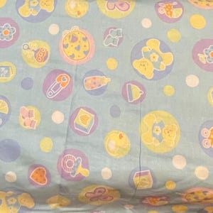 Pastelkleurige babykatoen – kinderkamerprint met teddyberen, rammelaars en flessen – zachte blauwe babyquiltstof op maat gesneden