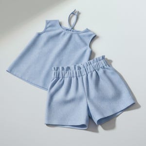 Puede incluir: Conjunto de dos piezas de punto acanalado azul claro, que incluye una camiseta sin mangas con cierre de lazo y pantalones cortos a juego con cintura elástica. El conjunto está hecho de un material suave y cómodo.