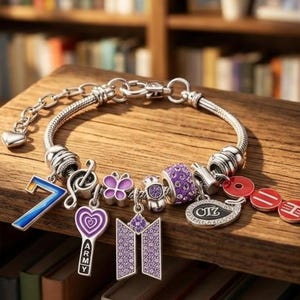 May include: A silver-toned charm bracelet featuring a variety of pendants including a blue gradient number 7, a purple heart-shaped charm with the text ARMY, a purple butterfly, a purple logo charm, a purple crystal bead, and red circular charms.