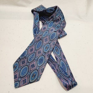 Peut inclure: Une cravate en soie à motif bleu et rose avec un design géométrique. La cravate a une extrémité pointue et est pliée en deux.