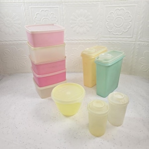 May include: A selection of vintage plastic food storage containers in pastel shades. The set features rectangular boxes in pink and beige, tall canisters in yellow and mint green, and smaller round and cylindrical containers.