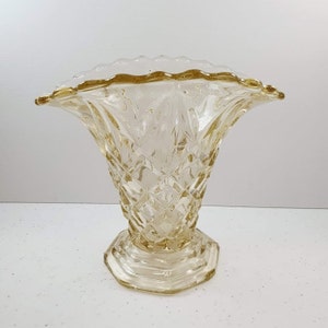 May include: A clear glass vase with a diamond pattern and a scalloped rim. The vase is a pale yellow colour.