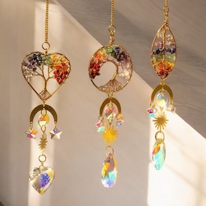 Puede incluir: Tres adornos de alambre dorado en forma de árbol de la vida con acentos de piedras preciosas arcoíris. Cada adorno tiene una forma diferente: corazón, círculo y óvalo. Cada adorno tiene un prisma de cristal colgando de él.