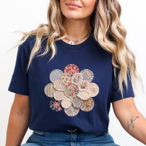 以下が含まれることがあります： ネイビーブルーのTシャツ。様々な柄の生地で作られた花の模様が特徴です。花のデザインはシャツの中央に配置され、花柄、ストライプ柄、無地など、円形のパッチで構成されています。Tシャツは半袖で、クルーネックです。