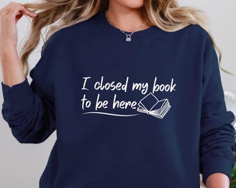 May include: A navy blue sweatshirt with the text "I closed my book to be here" in white lettering. A white outline of a closed book is next to the text.
