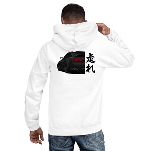 Op de afbeelding: Witte hoodie met een zwarte autografiek op de achterkant. De auto is in profiel afgebeeld, met Japanse karakters rechts. De hoodie heeft een capuchon met trekkoord en lange mouwen.