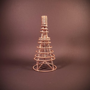 Puede incluir: Una escultura de alambre de color cobre con forma de torre cónica. La estructura está compuesta por hilos de metal trenzado que forman una serie de anillos concéntricos que disminuyen en diámetro hacia la parte superior, terminando en una punta.