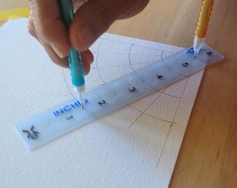 May include: A person using a clear ruler marked in inches to measure a drawing on white paper. A blue and a yellow pencil are used to draw arcs and lines. The ruler is marked with the word "INCHI".