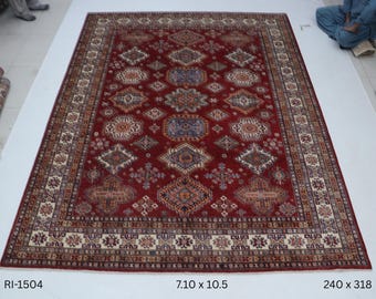 Puede incluir: Una alfombra roja rectangular grande con un intrincado patrón geométrico. La alfombra presenta un campo central de motivos repetidos de diamantes y flores en tonos de azul, beige y marrón. El borde es de color crema con patrones repetidos. La alfombra mide 216 cm x 320 cm.