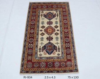 Könnte beinhalten: Rechteckiger beiger Teppich mit einem zentralen geometrischen Design in Rot, Blau und Gold. Der Teppich hat einen roten Rand mit sich wiederholenden Mustern. Maße: 2,5 x 4,3 Fuß und 190 x 330 cm.