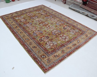 Könnte beinhalten: Ein rechteckiger, olivgrüner Teppich mit einem detaillierten Blumenmuster. Der Teppich hat einen roten Rand mit aufwendigen Designs und ein Mittelfeld mit stilisierten Blumen in Rot-, Blau- und Brauntönen. Der Teppich ist wahrscheinlich aus gewebtem Material.