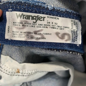 May include: Close-up of a blue denim Wrangler jeans label. The label reads "Wrangler 936DEN 36 X 32" and includes washing instructions. The jeans are made of 100% cotton and made in Mexico of US fabric.