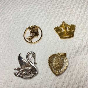 May include: Four vintage brooches and pendants. Includes a gold-tone crown pin, a gold-tone pendant with a heart-shaped filigree design, a silver swan pin, and a gold-tone pin with a profile of a woman.