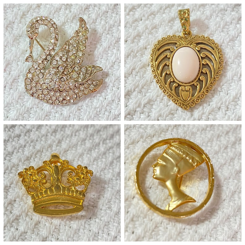 May include: Four pieces of jewelry: a rhinestone swan brooch, a gold heart pendant with a pink stone, a gold crown pin, and a gold circular pin with a profile of a woman.