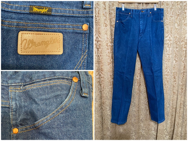 May include: Blue denim Wrangler jeans. The jeans have a classic five-pocket design with copper-coloured rivets and stitching. A leather patch with the Wrangler logo is visible on the back pocket. The jeans are hanging on a hanger.