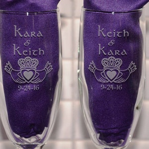 May include: Two clear glass champagne flutes featuring etched designs. One glass is engraved with the names Kara & Keith, the other with Keith & Kara, both including a Claddagh symbol and the date 9-24-16. Each glass contains a purple fabric insert.