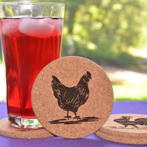 May include: Four round cork coasters with a black silhouette of a chicken on each. The coasters are stacked on top of each other. A glass of red iced tea is in the background.