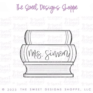 May include: A black and white line drawing of a stack of books with the text "Mrs. Simon" on the middle book. The drawing is on a white background with a watermark of "The Sweet Designs Shoppe".