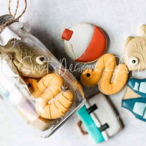 May include: A glass jar filled with various cookies decorated with fishing-themed designs, including a fish, a worm, and a bobber. The cookies are arranged around a clear glass jar with a metal lid.