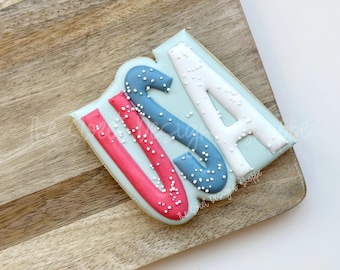 May include: A cookie decorated with red, white, and blue icing, spelling out "USA" with white sprinkles on top.