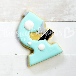 May include: A blue and white cookie shaped like a microscope. The cookie has white dots on it.