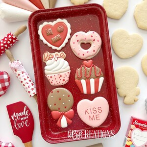 May include: A red baking sheet with nine Valentine's Day themed sugar cookies. The cookies are decorated with pink, red, white, and brown frosting and sprinkles. The cookies are shaped like hearts, cupcakes, lollipops, and donuts. The baking sheet has a red speckled finish and the text "6B CREATIONS" is printed on the bottom.