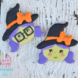 May include: Two decorated sugar cookies shaped like witches with purple hair, black hats, and orange bows. The witch on the left is wearing glasses.