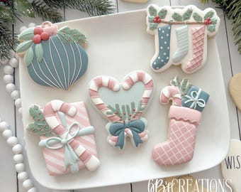 May include: A plate of decorated Christmas cookies with a blue and white striped ornament, a pink and white striped gift box with a candy cane, a heart-shaped cookie with candy canes and a bow, a pink stocking with a candy cane and a gift, and three stockings hanging from a branch.