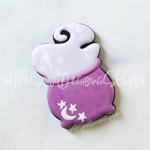May include: Purple cauldron cookie decorated with white icing and stars. The cauldron has a white cloud of smoke coming out of the top.