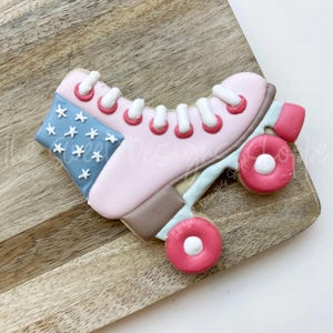 May include: A pink and blue decorated sugar cookie shaped like a roller skate with white laces and red wheels.