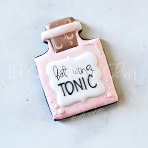 May include: A pink and brown cookie shaped like a bottle with a white label that says "bat wing tonic".
