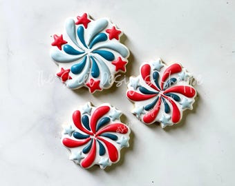 May include: Three sugar cookies decorated with red, white, and blue frosting in a firework design. The cookies are on a white background.