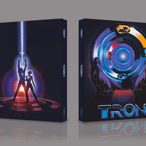 May include: Two Blu-ray cases for the film "TRON". One shows a blue light beam and figures, the other a circular design. The film's title is at the bottom. The cases are on a grey surface.