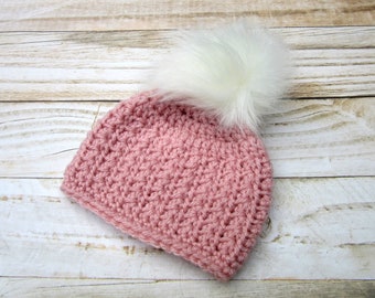 Könnte beinhalten: Eine rosa gestrickte Mütze mit einem weißen Kunstfellbommel.